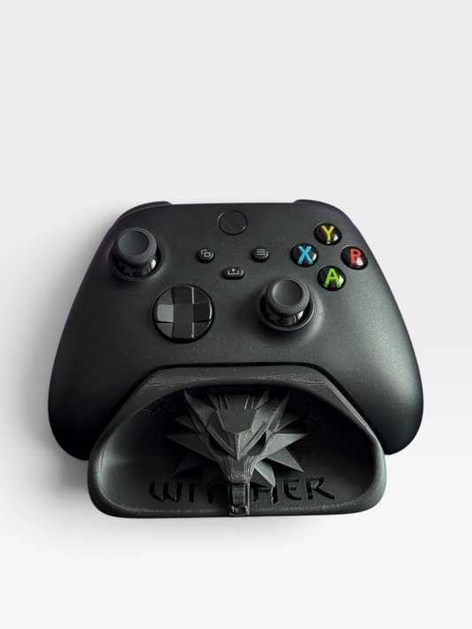 A matte black game controller dock designed for a Xbox-style controller, featuring the Witcher logo and the word 'WITCHER' embossed on the front, shown on a light gray background.