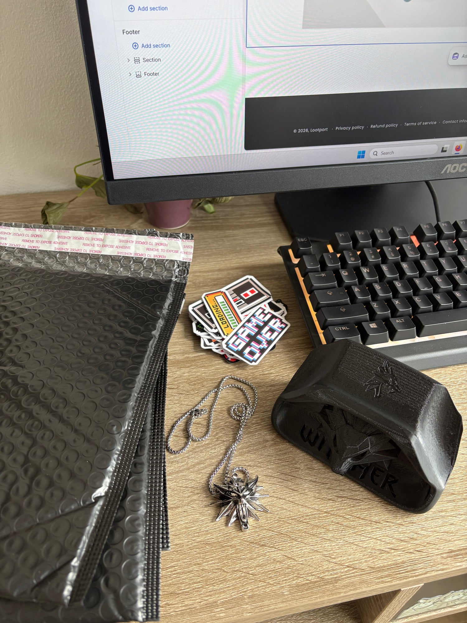 Close-up of a desk with a computer, keyboard, and various items including a necklace and stickers.